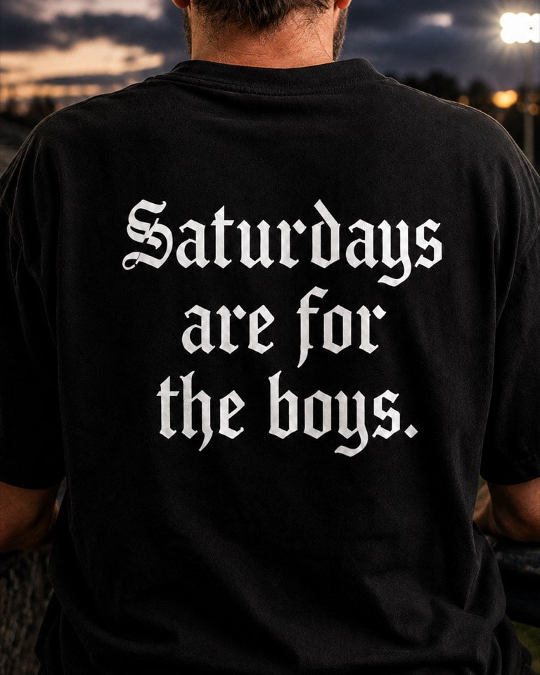 Man at a floodlit football field wearing a black YapThreads Saturdays Are For The Boys tee