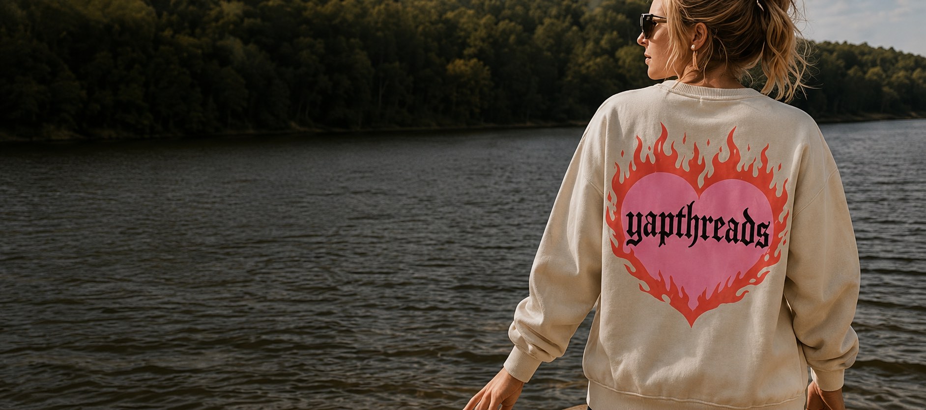 Woman by a lake wearing a cream YapThreads crewneck with a flaming heart print