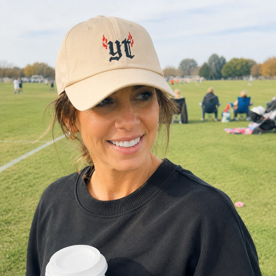 Mom smiling at a sunny soccer field in the cream yt embroidered cap and a black YapThreads sweatshirt